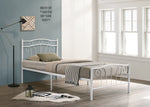 White metal bed frame with bedding in a room with large windows and a lamp.