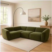 Green sectional sofa in a living room with a lamp, plant, and painting.